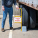 A person using a yellow Vestil aluminum wheel chock with a sign on the side of a truck.