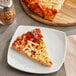 A slice of pizza on a plate with red pepper flakes.