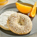 A plate with a bagel with white cream cheese and Hometown Provisions white sesame seeds with orange slices on the side.