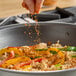 A hand sprinkling Hometown Provisions cayenne pepper on food in a pan.