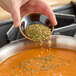 A person pouring Hometown Provisions dried oregano into a bowl of soup.