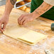 A person's hand rolling Grassland unsalted butter sheet on a wooden surface.