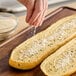 A person sprinkling Hometown Provisions garlic powder on a loaf of bread.