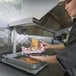 A woman holding a basket of fries over a heated food warmer.