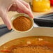 A person pouring Hometown Provisions Cajun Spice into a pot of soup.