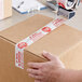 A person using Tape Logic "Stop / If Seal is Broken" tape to seal a cardboard box.
