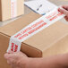 A person using Tape Logic "Mixed Merchandise" packing tape to seal a box.