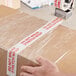A person using Tape Logic "Do Not Break Stretch Wrap" to seal a box.