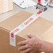 A hand using Tape Logic "Caution / If Seal is Broken" carton sealer tape to seal a box.