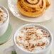 Two cups of coffee with cinnamon rolls on a white table with a Hometown Provisions Ground Cinnamon pastry.
