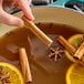 A person holding Hometown Provisions cinnamon sticks over a pot of brown liquid.