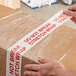 A person using Tape Logic "Do Not Break Stretch Wrap" to seal a box.