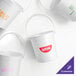 A group of white Howw Manufacturing plastic drink buckets with clear handles, each with a different logo.