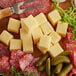 A block of Alps Natural Gruyere cheese on a cutting board with meat.