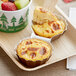 A tray with Artisan Kitchens Bacon and Three Cheese Egg Bites and a bowl of fruit on a table.