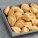 A tray of Cuisine Innovations chicken empanadas on a gray surface.