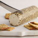 A knife cutting a block of Celebrity Goat Garlic and Herb Goat Cheese.