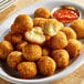 A plate of Simply Cuisine Smoked Gouda Arancini on a table with a bowl of sauce.