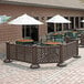 A white umbrella with a round top on a table in an outdoor patio area with Grosfillex fence posts and a brown table and chairs.