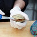 A person in white gloves holding a clam shell and cutting it with a Victorinox clam knife.