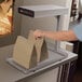 A person holding a brown bag of food over a heated Hatco Ultra-Glo food warmer.