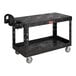 A black Rubbermaid® plastic utility cart with two flat shelves and wheels.