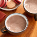 Two cups of Cocoa Classics Chocolate Supreme hot chocolate on a table with macarons.