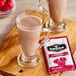 A glass of pink raspberry and chocolate cocoa next to a Cocoa Classics Raspberry and Chocolate Cocoa mix packet.
