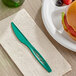 A Stalk Market green compostable knife on a white surface next to a plate with a sandwich.