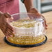 A person holding a cake with a clear plastic scalloped lid.