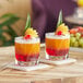 Two glasses of colorful drinks garnished with fruit on a table with coasters.
