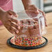 A person holding a cake with a clear plastic scalloped lid.