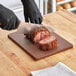 A person wearing black gloves cutting meat on a brown Choice polyethylene cutting board.