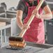 A woman in a red apron using a Choice double head carbon steel bristle grill brush to clean a grill.