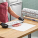 A person in a red apron and black gloves using Choice barbecue print butcher paper to wrap a piece of meat.