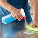 A person using a red Lavex spray bottle to clean a table.