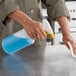 A person using a Lavex yellow sprayer to clean a professional kitchen counter with blue liquid.