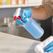 A person in blue gloves using a red spray trigger on a Lavex plastic bottle.