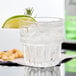 A Libbey Everest rocks glass filled with clear liquid, ice, and a lime wedge.