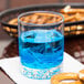 A Libbey Nob Hill rocks glass with blue liquid and ice on a table next to pretzels.