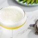 A glass of yellow liquid with a lime wedge and a metal spoon on the table.