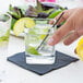 A hand holding a Libbey Rocks glass of water with ice and lime slices.