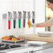 A woman using Fourt&#233; stainless steel scalloped tongs with color coated handles in a professional kitchen.