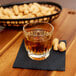 A Libbey Winchester rocks glass filled with brown liquid on a table with a bowl of peanuts.