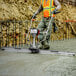 A man in a safety vest using a Tomahawk concrete power screed to level concrete.