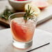 A Libbey rocks glass of a drink with ice and a sprig of rosemary.