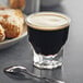 A Libbey Gibraltar espresso glass filled with dark liquid with a spoon and pastries on a plate on a table.