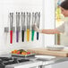 A woman wearing gloves and holding Fourt&#233; stainless steel scalloped tongs with color coated handles in a professional kitchen.