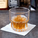 A Libbey Everest rocks glass with a drink and ice sits on a table next to a bottle of whiskey.
