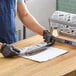 A person in a blue apron and black gloves cutting fresh fish on a table with Choice Fresh Catch Butcher Paper on the counter.